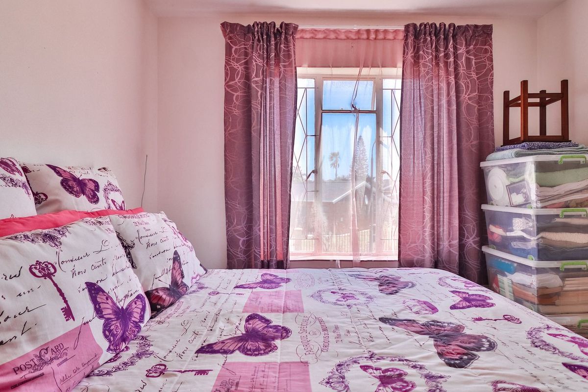 A bedroom featuring a window with security bars and curtains, providing natural light and a view of the exterior.