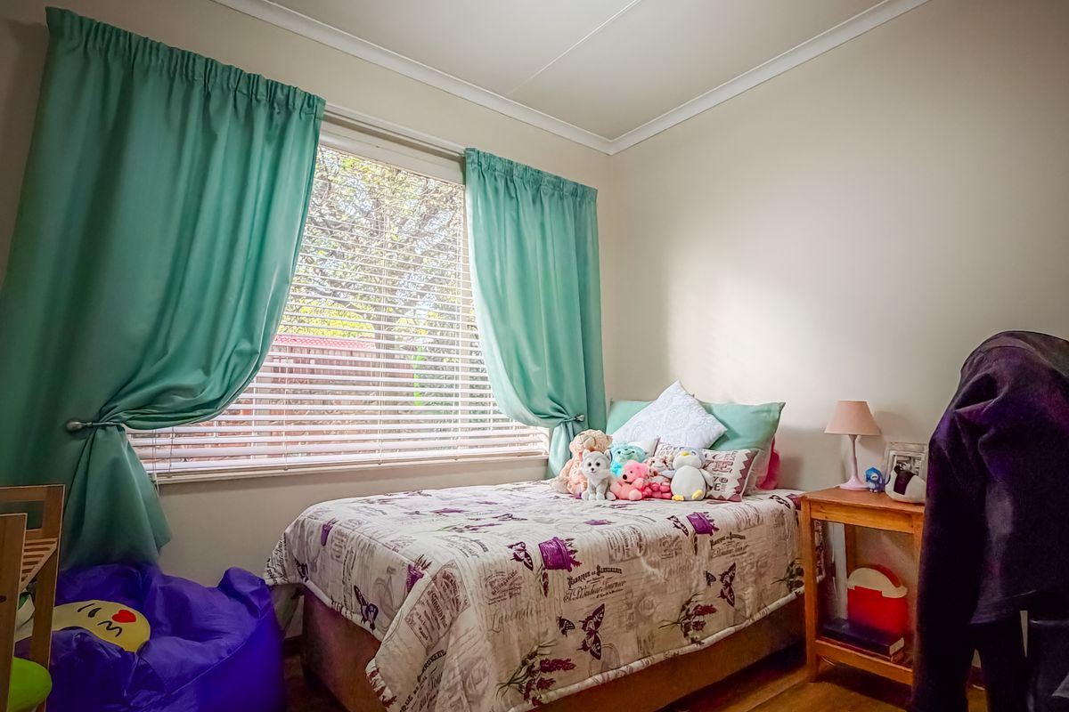 A cozy bedroom featuring laminate flooring, a window with venetian blinds, and a central ceiling light fixture.