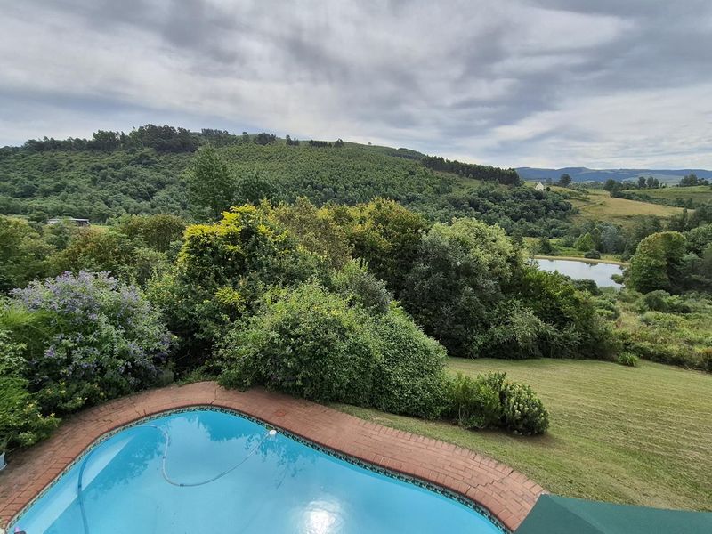 An outdoor swimming pool with brick coping overlooking a scenic rural landscape with rolling hills and a small dam.