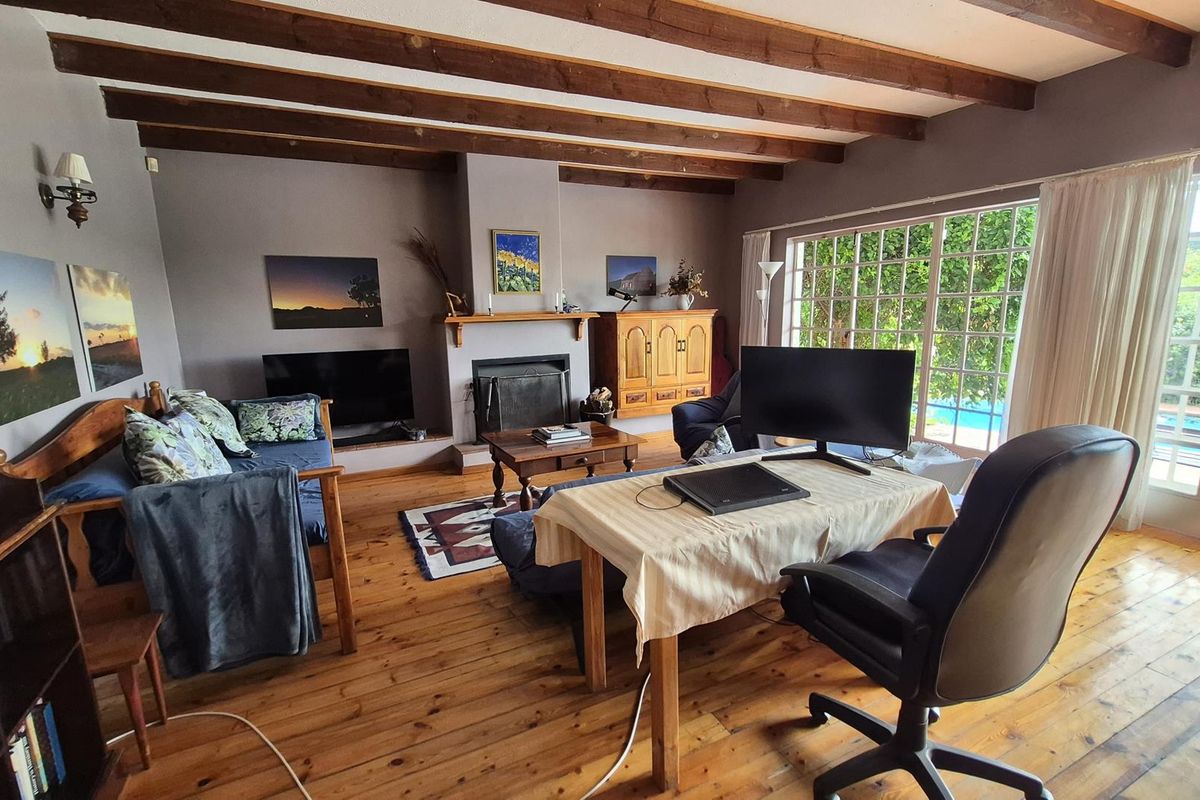 Spacious living room featuring exposed timber ceiling beams, warm hardwood flooring, and a built-in fireplace, with large glass doors providing natural light and garden access.