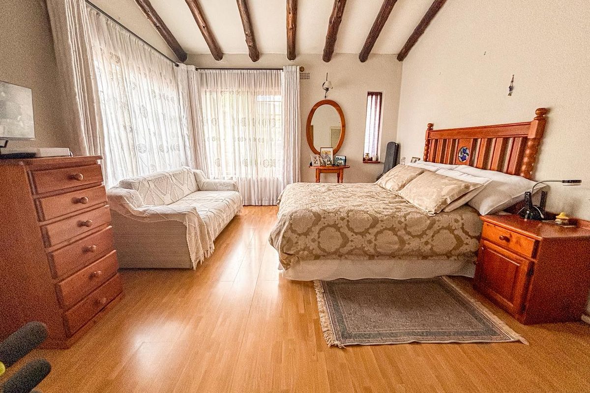 Spacious bedroom featuring exposed timber ceiling beams, laminate wood flooring, and large windows with natural light.