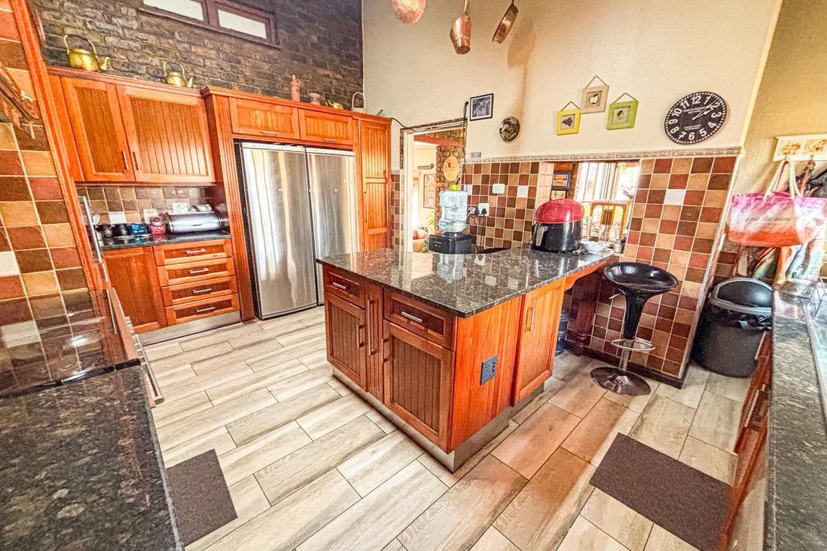 A spacious kitchen featuring wooden cabinetry, granite countertops, a central island, and a distinctive exposed brick feature wall.