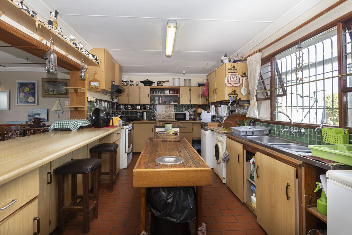 A functional kitchen featuring laminate cabinetry, terracotta flooring, a double basin sink, and a central island, offering potential for a modern renovation.