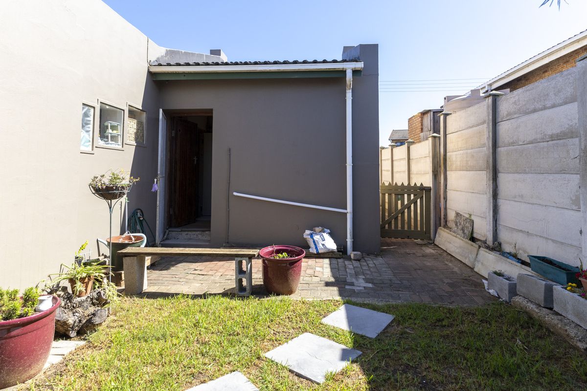 A compact rear courtyard featuring paved patio space, a small lawn, and secure boundary walling with a side access gate.