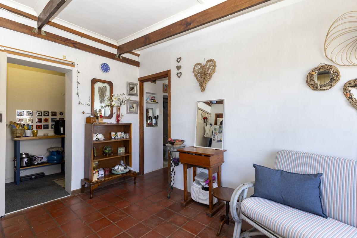 Living area featuring rustic exposed timber ceiling beams and traditional terracotta floor tiles, with an adjacent utility space and built-in wall niche.