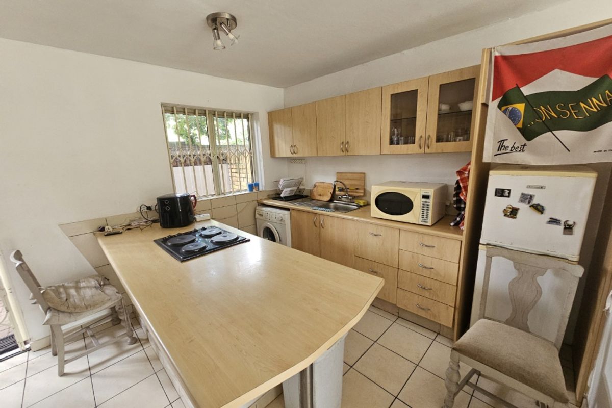 Functional kitchen featuring light wood cabinetry, laminate countertops with an integrated hob, tiled flooring, and a window with security bars.