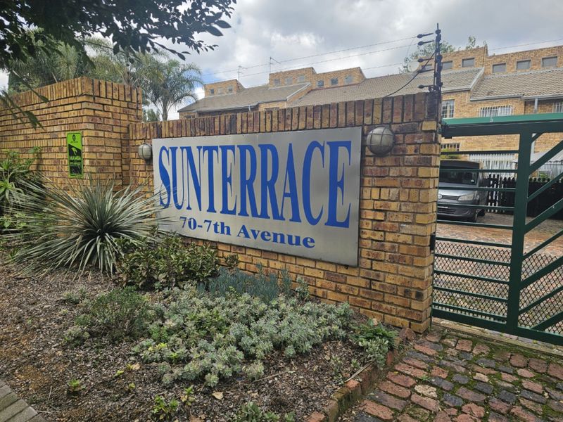 Front entrance view of the Sunterrace complex, featuring a brick boundary wall, security gate, and electric fencing.