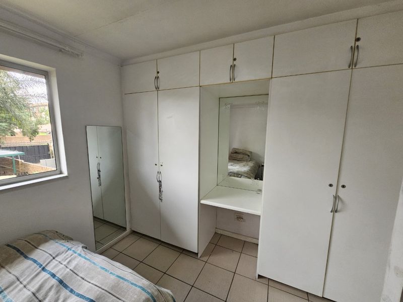A bedroom featuring extensive built-in cupboards with an integrated vanity area and tiled flooring.