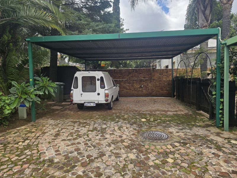 A covered carport area featuring a brick boundary wall and cobblestone paving, providing secure off-street parking.