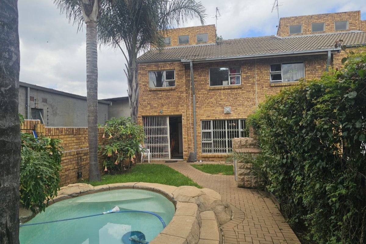 Rear view of the cluster property featuring a private swimming pool, paved walkway, and established garden area with brick facade.