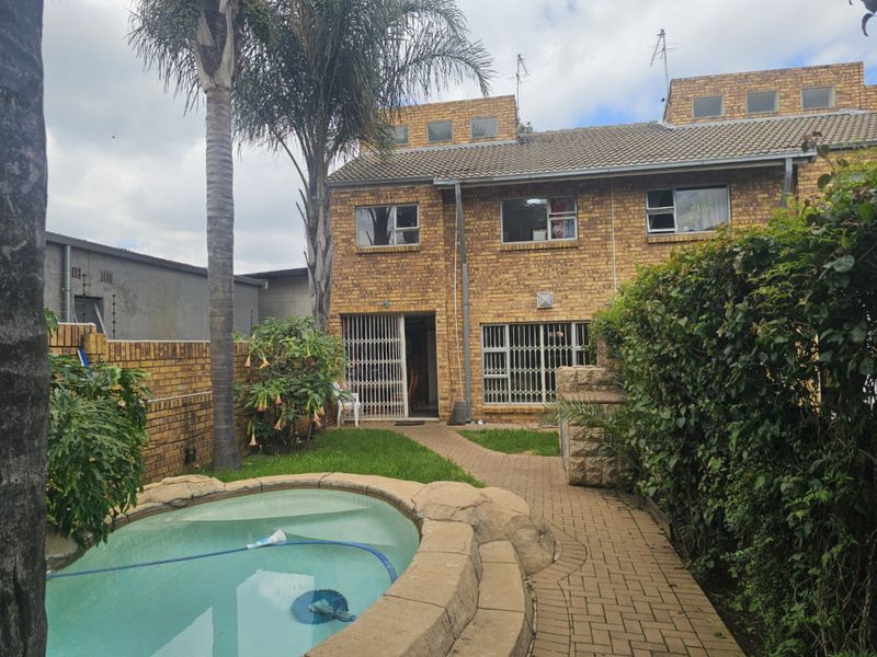Rear view of the cluster property featuring a private swimming pool, paved walkway, and established garden area with brick facade.