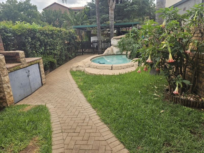 Private garden area featuring a rock-style splash pool, paved walkway, and a built-in brick braai facility, ideal for outdoor entertaining.