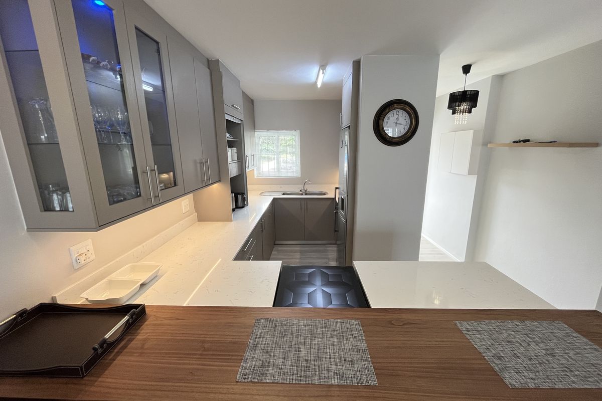 Modern kitchen featuring sleek grey cabinetry, quartz countertops, a breakfast bar, and integrated lighting, offering a clean and functional culinary space.