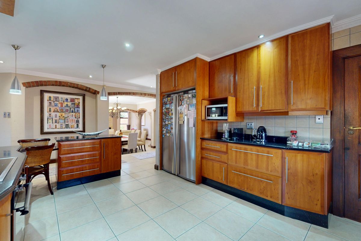 Spacious kitchen featuring warm wooden cabinetry, granite countertops, and tiled flooring, seamlessly flowing into the adjacent dining area through a decorative brick archway.