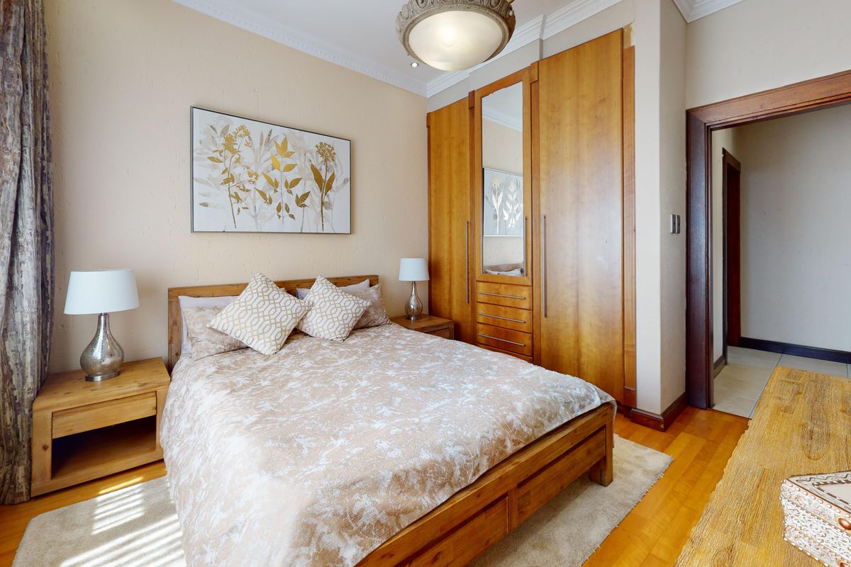 A well-maintained bedroom featuring warm hardwood flooring, coving, and extensive built-in wooden cabinetry with an integrated mirror.