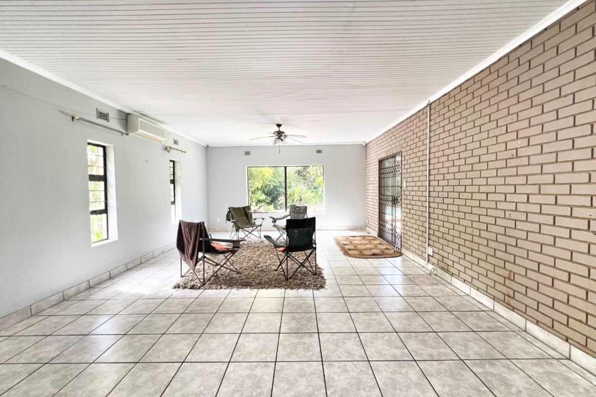 Spacious living area featuring tiled flooring, an exposed brick feature wall, ceiling fan, and split system air conditioning.