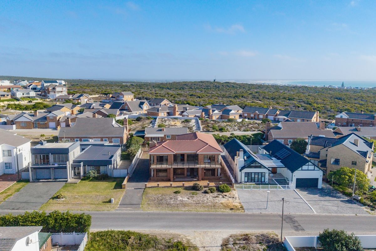 Aerial view of a residential coastal neighborhood featuring a two-story house with a tiled roof and balcony, surrounded by similar suburban properties.