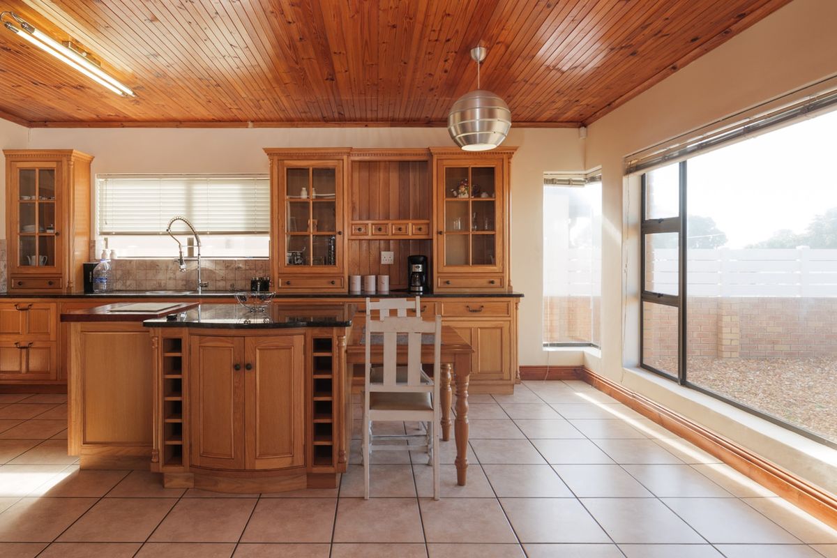 Spacious kitchen featuring warm timber cabinetry, granite countertops, a central island with wine storage, and a distinctive timber tongue and groove ceiling.