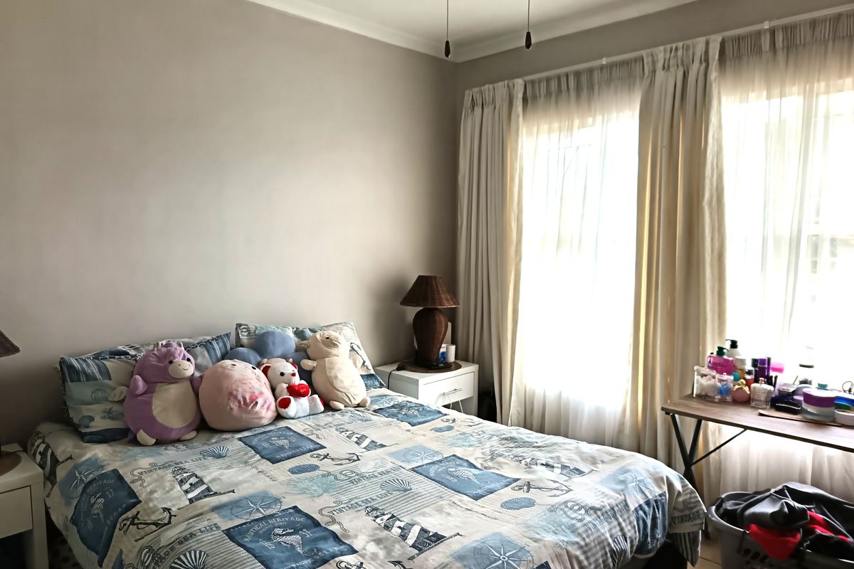 A well-lit bedroom featuring neutral wall tones, a ceiling fan, and large windows dressed with floor-to-ceiling curtains.