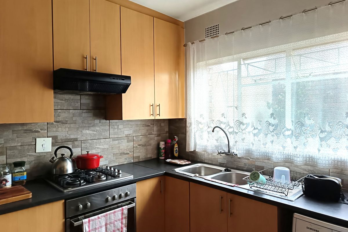 A functional kitchen featuring light wood cabinetry, a gas hob, built-in oven, extractor fan, and a double stainless steel sink with tiled splashback.