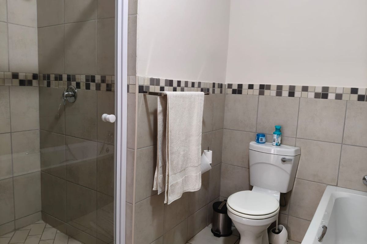 A functional bathroom featuring a separate shower enclosure, bathtub, and toilet with neutral ceramic wall tiling and a decorative mosaic border.