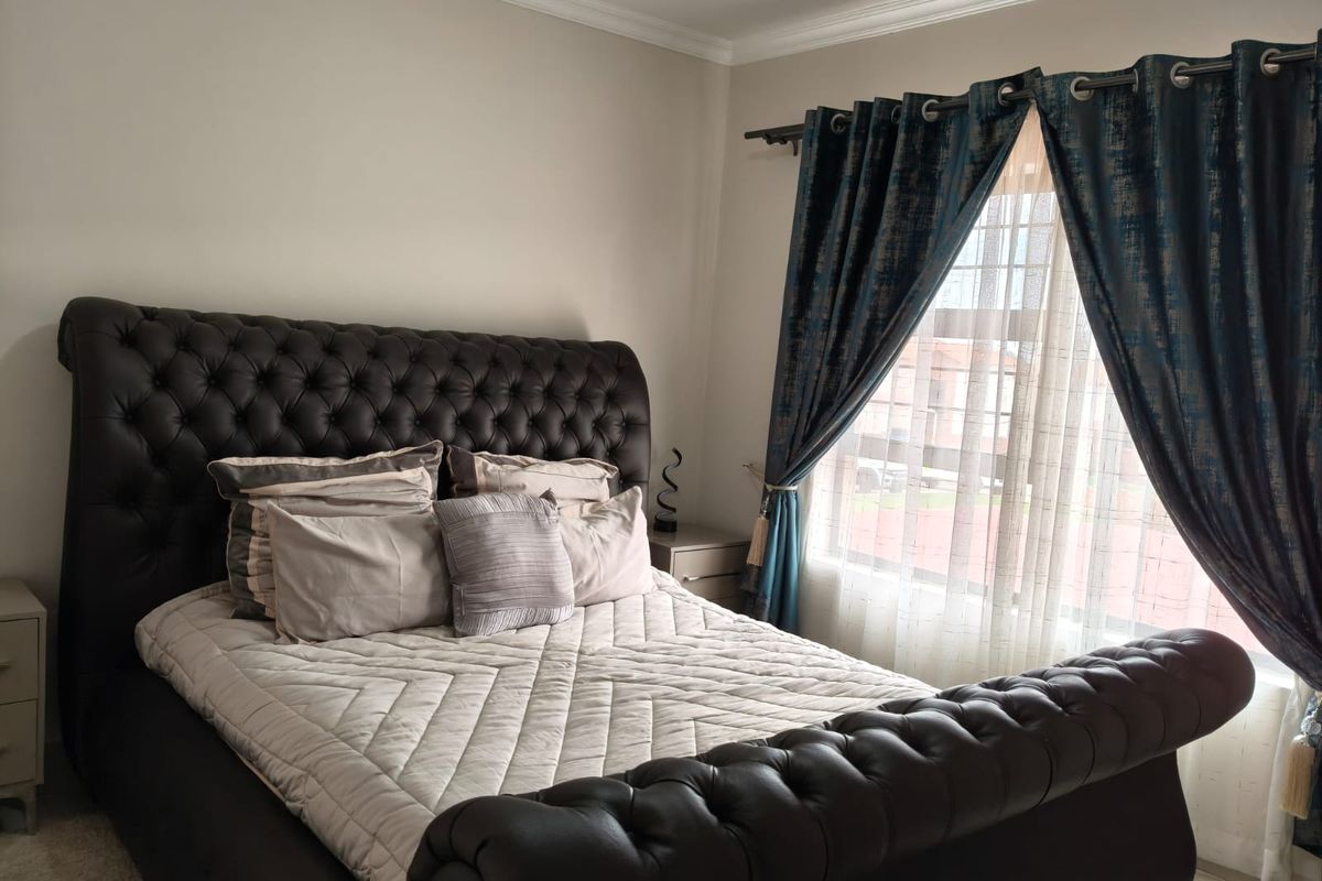A well-maintained bedroom featuring neutral wall finishes, coving, and a window dressed with decorative curtains.