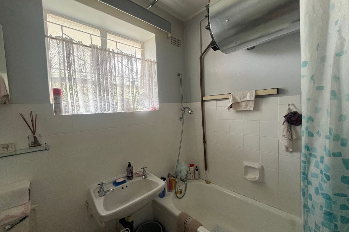 Compact bathroom featuring a bathtub, wall-mounted basin, and an exposed electric water heater unit.
