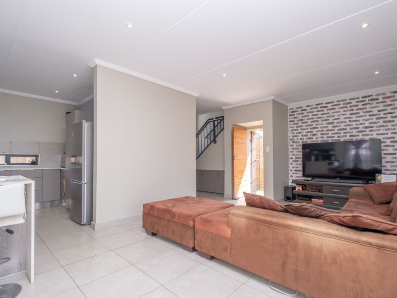 An open-plan living and kitchen area featuring modern tiled floors, an exposed brick feature wall, and recessed lighting, creating a bright and functional living space.