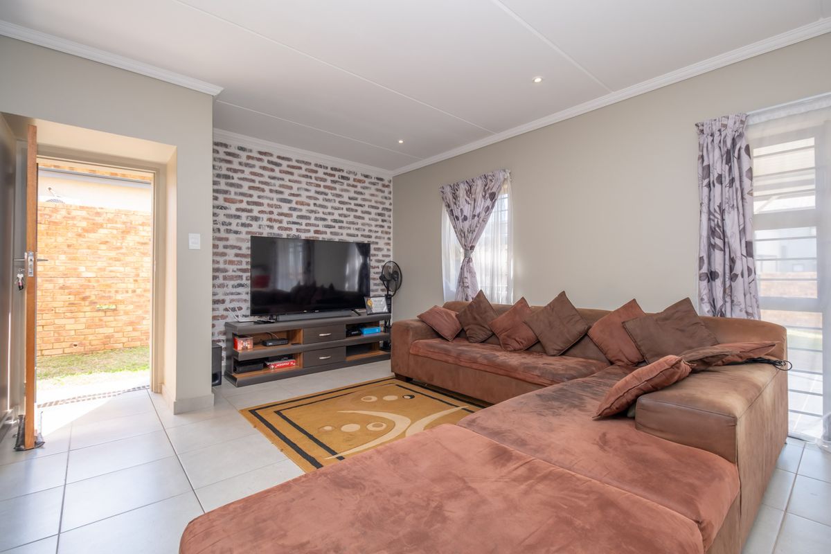 A comfortable living room featuring an exposed brick accent wall, tiled flooring, and direct access to an outdoor area.