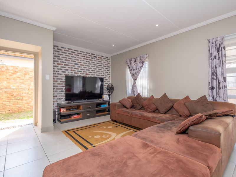 A comfortable living room featuring an exposed brick accent wall, tiled flooring, and direct access to an outdoor area.