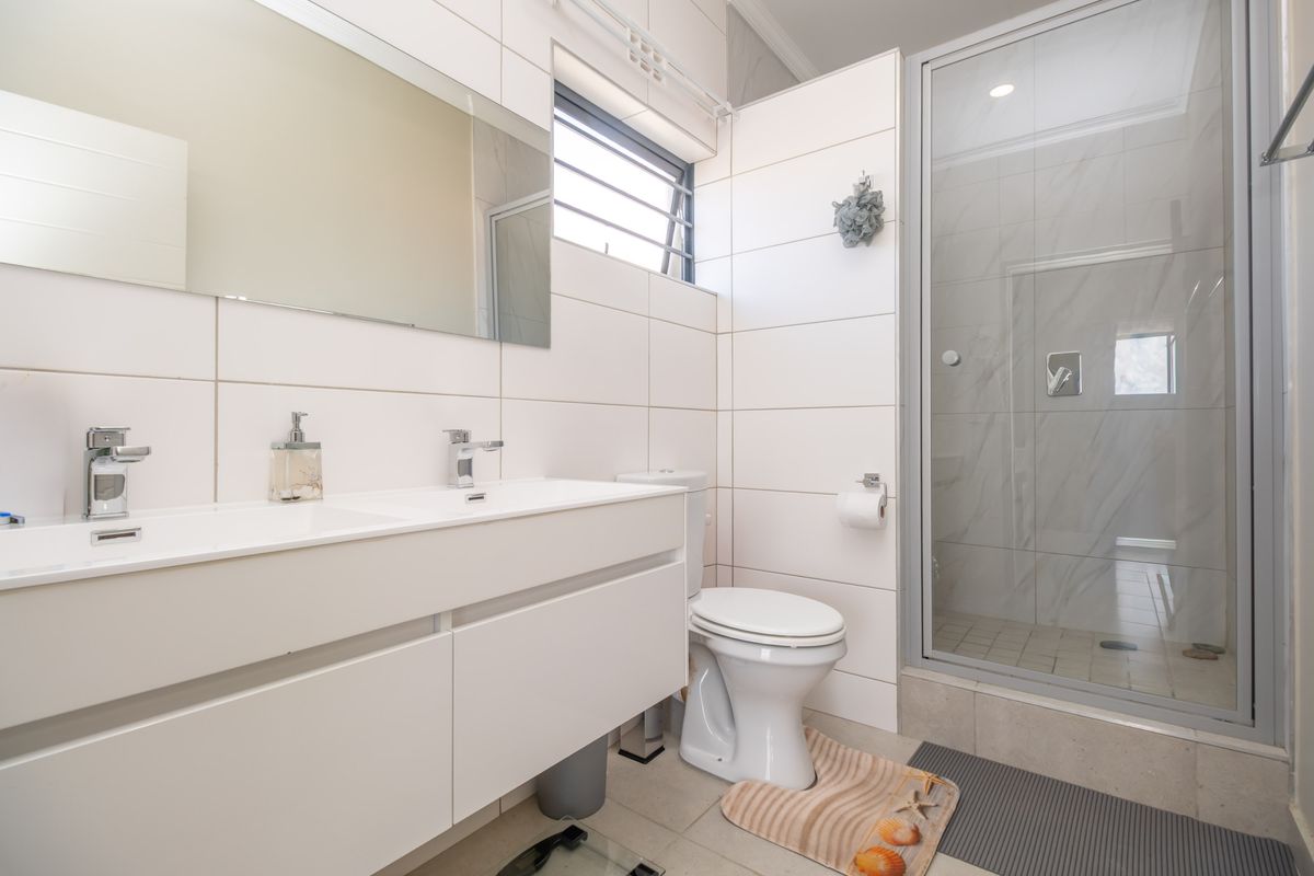 Modern bathroom featuring a double vanity, large wall mirror, toilet, and a glass-enclosed shower with neutral tiled finishes.