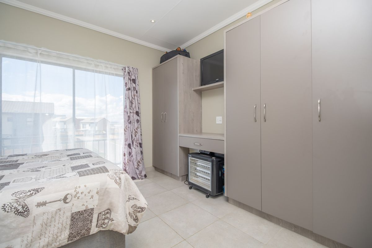 A well-maintained bedroom featuring neutral tiled flooring, built-in cabinetry with integrated storage, and a sliding glass door providing natural light and balcony access.