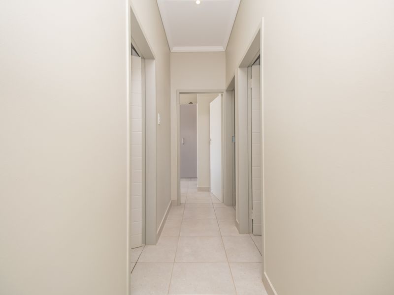 A clean, neutral-toned hallway featuring tiled flooring, coved ceilings, and recessed lighting, providing access to multiple rooms.