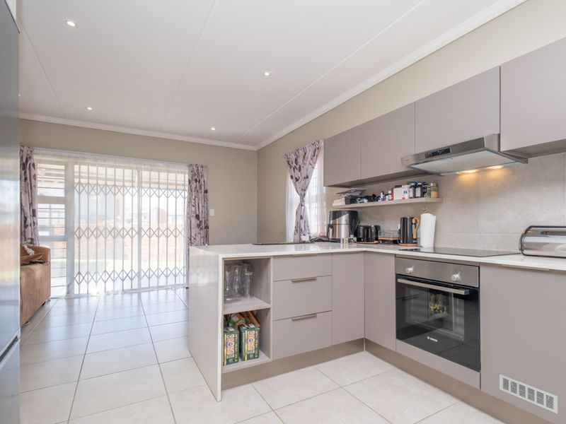 Modern kitchen featuring sleek cabinetry, built-in oven, electric cooktop, and tiled flooring, with direct access to the outdoor area through a sliding glass door.