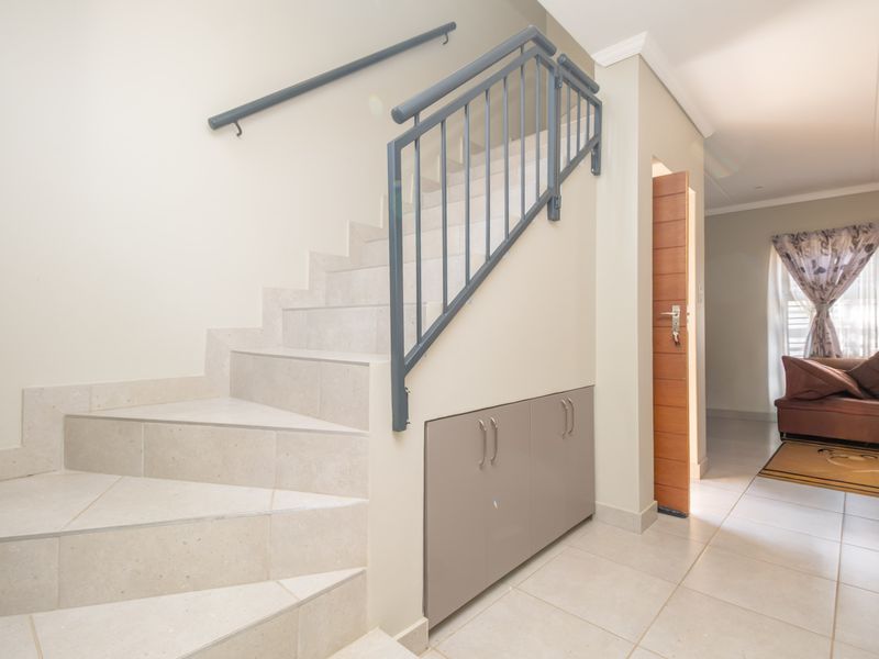 Entrance area featuring a tiled staircase with a metal handrail, integrated under-stair storage cabinetry, and neutral floor tiling leading into the living space.