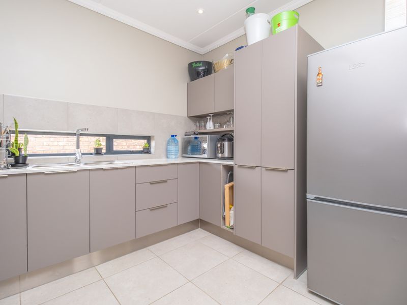 A modern, well-maintained scullery featuring sleek grey cabinetry, a stainless steel sink, tiled splashback, and neutral floor tiles.