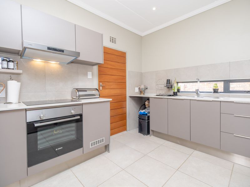 Modern kitchen featuring sleek grey cabinetry, stone countertops, built-in oven, electric hob, and a tiled backsplash with a functional layout.