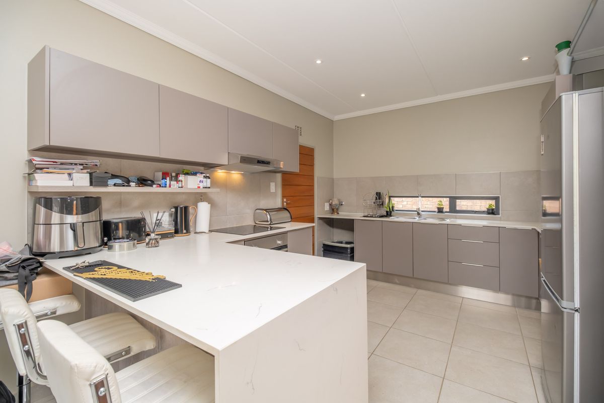 Modern kitchen featuring sleek grey cabinetry, quartz countertops, integrated appliances, and tiled flooring with recessed lighting.