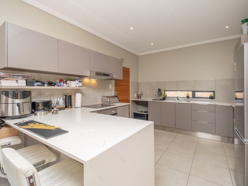 Modern kitchen featuring sleek grey cabinetry, quartz countertops, integrated appliances, and tiled flooring with recessed lighting.