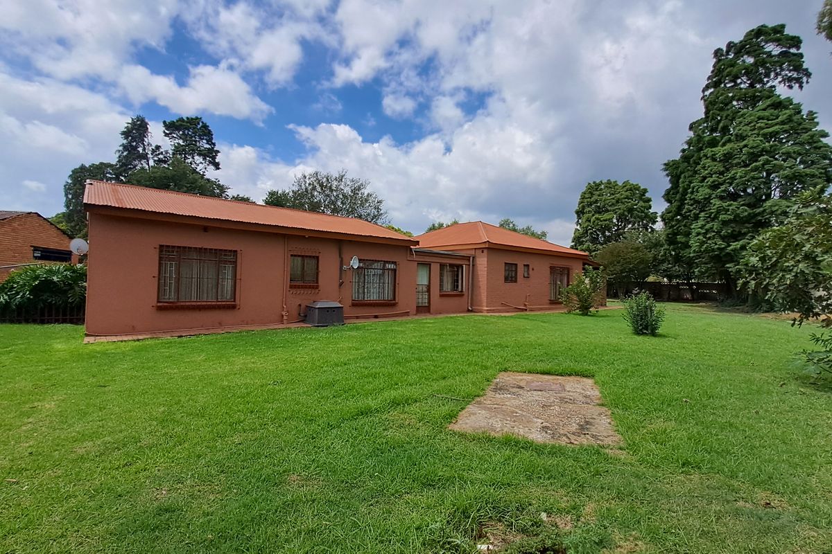 Rear view of the property showing the brick exterior, corrugated metal roof, security bars on windows, and a spacious surrounding lawn area.