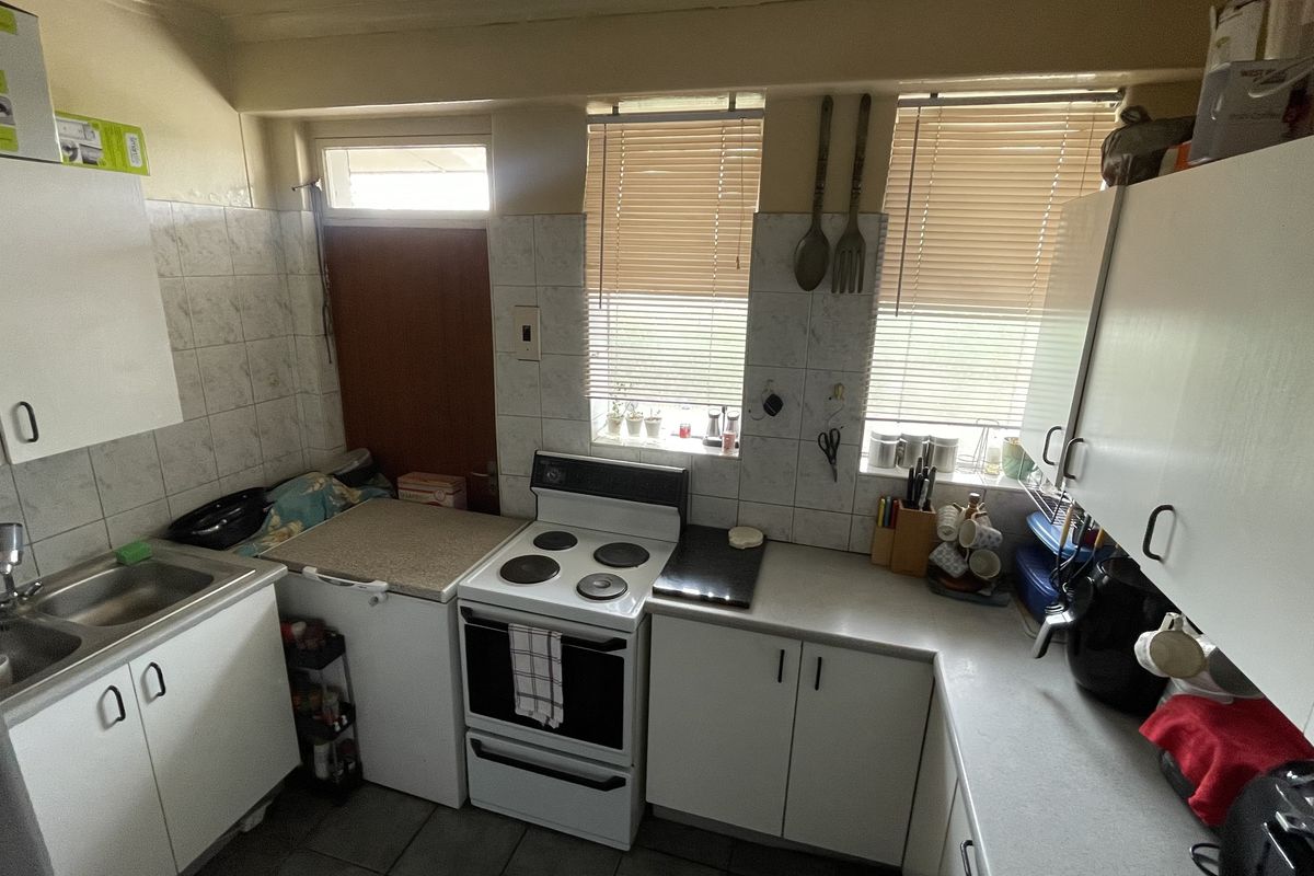 A compact kitchen featuring white cabinetry, laminate countertops, a stainless steel double sink, and a freestanding electric stove with tiled splashbacks.