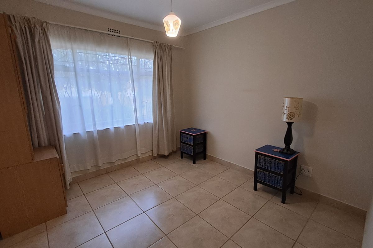 A simple, neutrally painted bedroom featuring tiled flooring, a window with security bars, and cove cornicing.