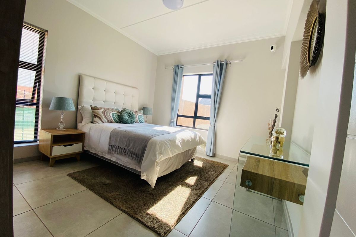 A bright and well-maintained bedroom featuring neutral tiled flooring, large windows for natural light, and a clean, modern aesthetic.