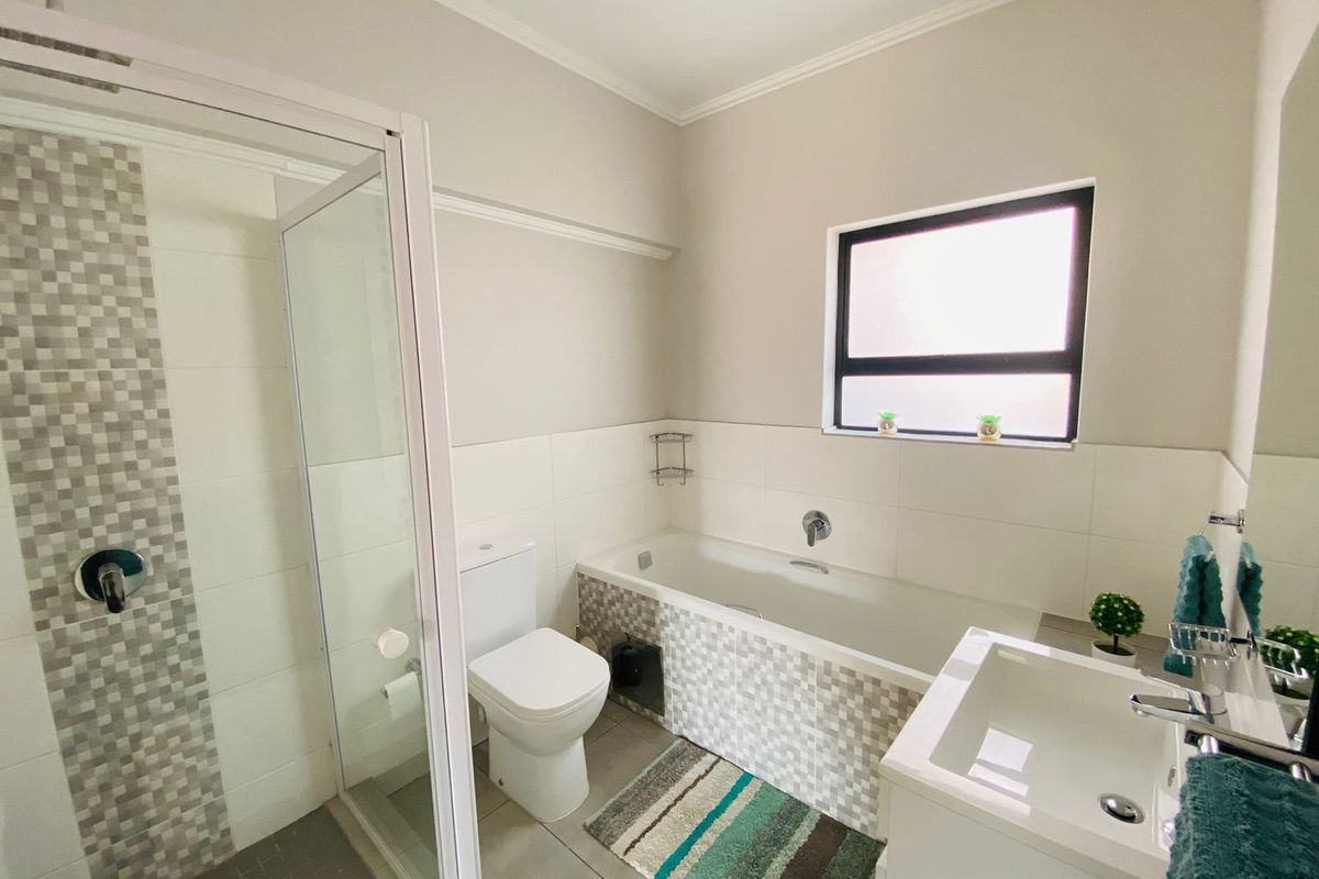 A well-maintained bathroom featuring a glass-enclosed shower, a bathtub with mosaic tile detailing, a vanity basin, and a toilet.