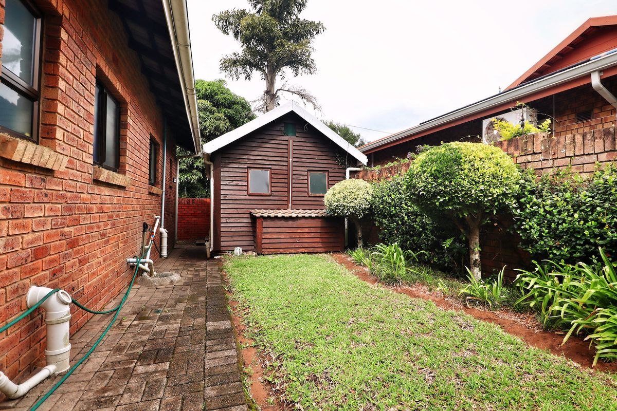 A side garden area featuring a paved walkway, a small timber shed, and established perimeter landscaping between two brick residential structures.