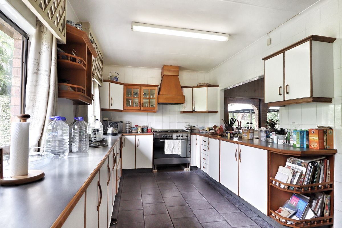A functional kitchen featuring wooden cabinetry, tiled splashbacks, a built-in oven with extractor hood, and dark floor tiles.