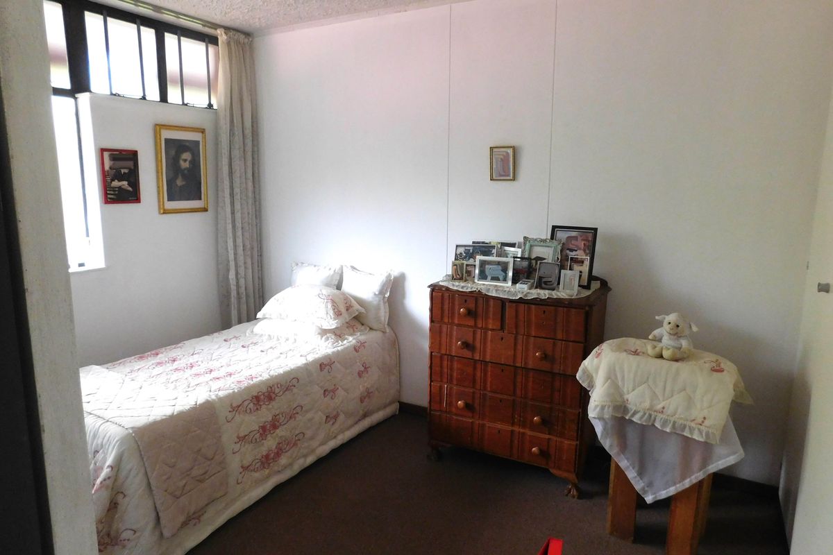A functional bedroom featuring a textured ceiling and a window fitted with security bars, providing a simple and practical living space.