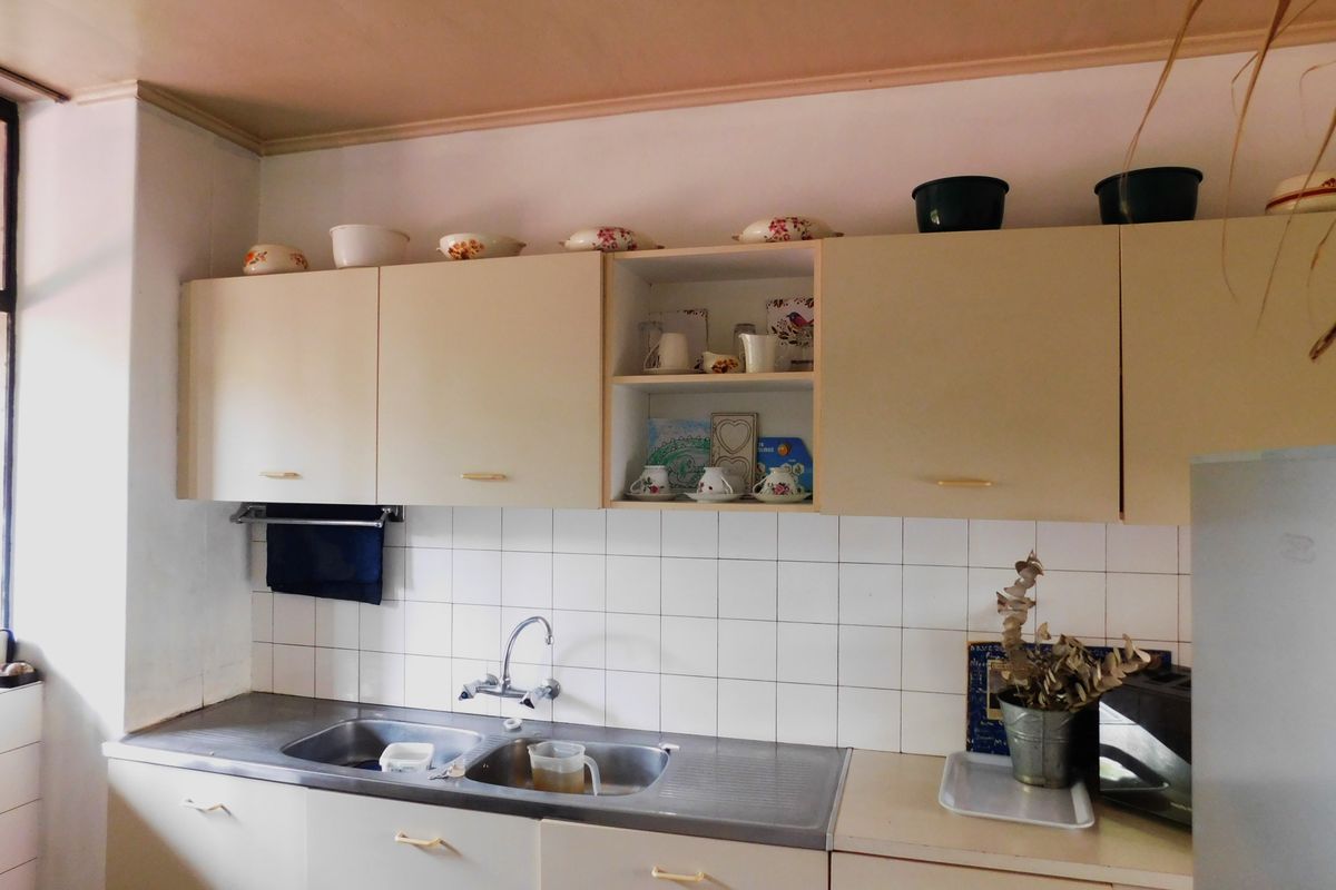 A functional kitchen featuring dated built-in cabinetry, a stainless steel double sink, and a tiled backsplash.
