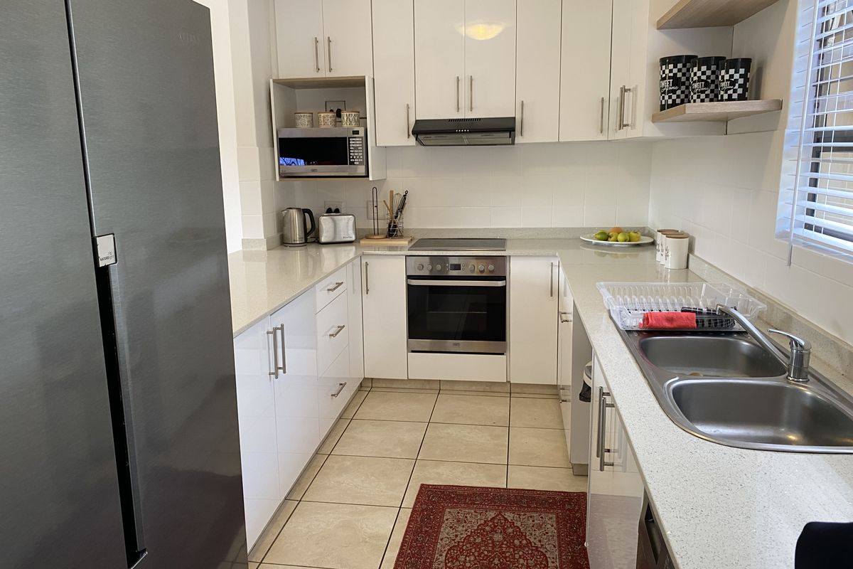 Modern kitchen featuring white gloss cabinetry, stone countertops, built-in oven, electric hob, extractor fan, and a double stainless steel sink.