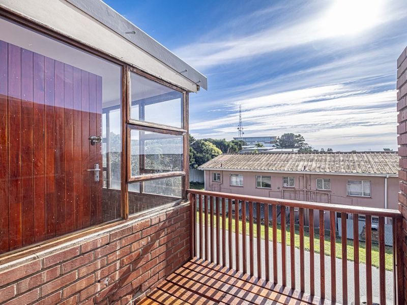 An elevated balcony featuring brick walls and a timber balustrade, offering an open outdoor space with views of the surrounding neighborhood.